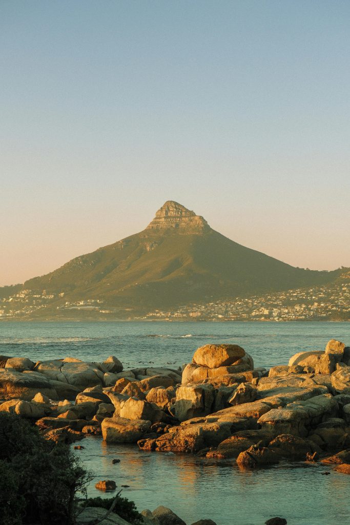 Scenic view of Lion's Head mountain from a rocky beach in Cape Town at sunset.
